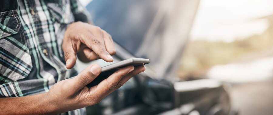 Man using smartphone with a broken down car in the background