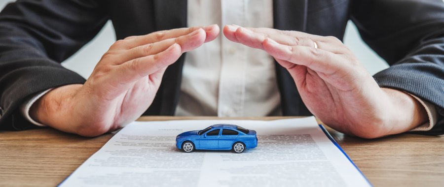 Two hands over a toy car on a table to represent car insurance