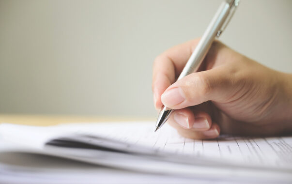 person holding pen next to paperwork