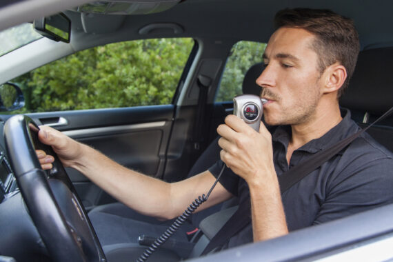 man blowing into breathalyzer in car