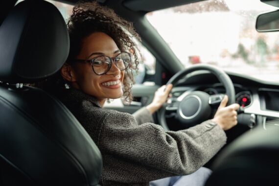 Smiling woman drives car and both hands are on steering wheel