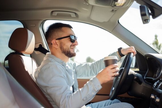 Happy man with coffee behind the wheel