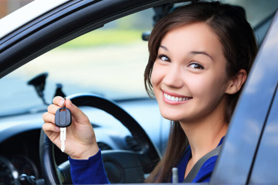 Smiling young lady holds keys while sitting in her car