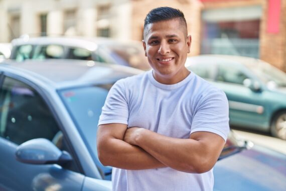Younf Latin man smiling in front of his car