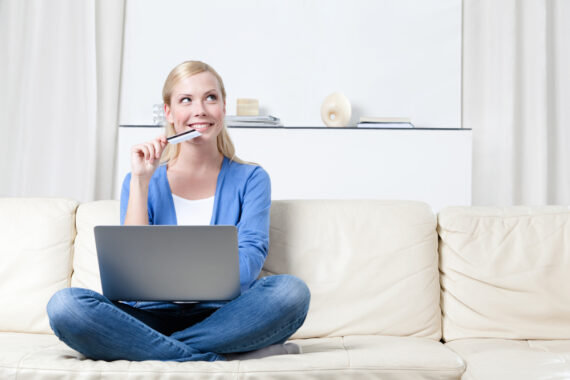 Happy young woman sitting on couch with credit card buying SR-22 insurance online.