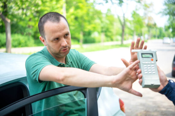 Man holds out his hands while police officer holds out a breathalyzer test.